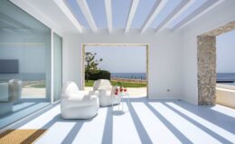 Modern coastal living room with white furniture, large glass windows, and stunning ocean views, showcasing a bright and airy atmosphere.