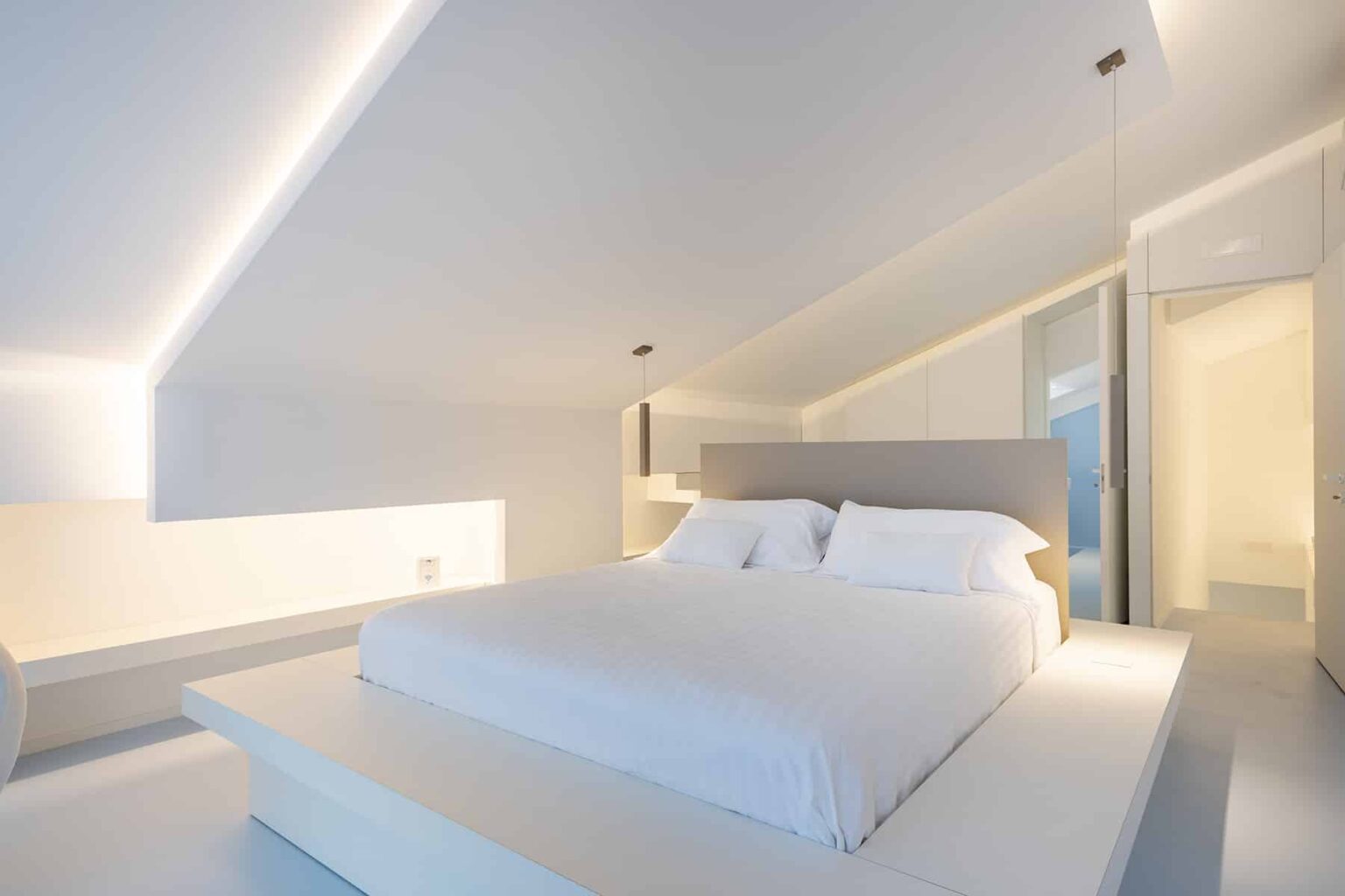 Modern minimalist bedroom featuring a large white bed with crisp linens, soft ambient lighting, and a sleek design. The room emphasizes clean lines and a spacious feel, ideal for relaxation and comfort. | Only on SopranoVillas
