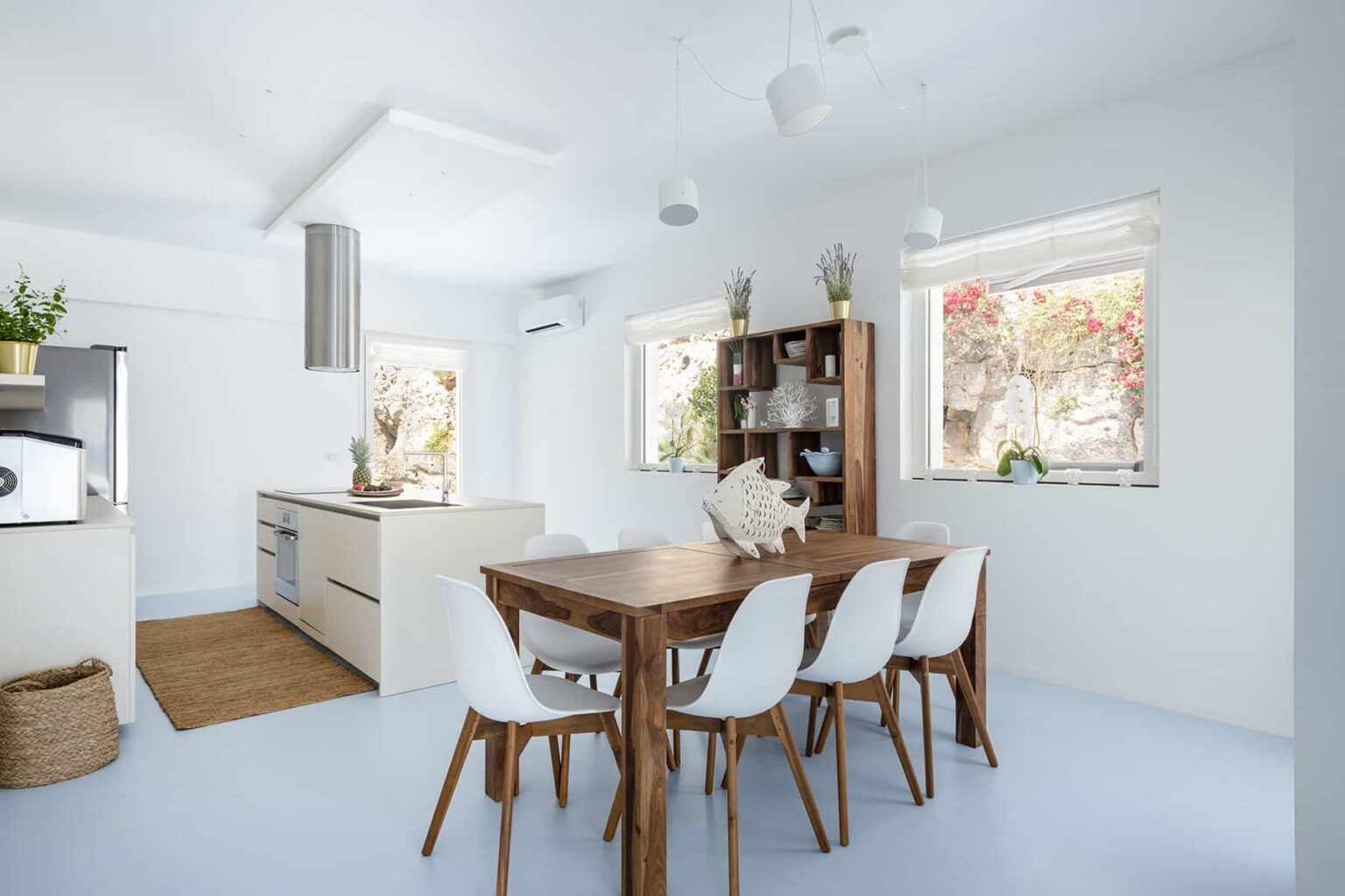 Modern open-concept kitchen and dining area featuring a wooden dining table with white chairs, a sleek kitchen with minimalist cabinetry, large windows allowing natural light, and a cozy atmosphere. | Only on SopranoVillas