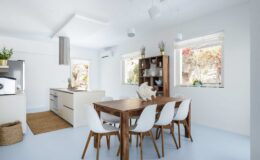 Modern open-concept kitchen and dining area featuring a wooden dining table with white chairs, a sleek kitchen with minimalist cabinetry, large windows allowing natural light, and a cozy atmosphere.