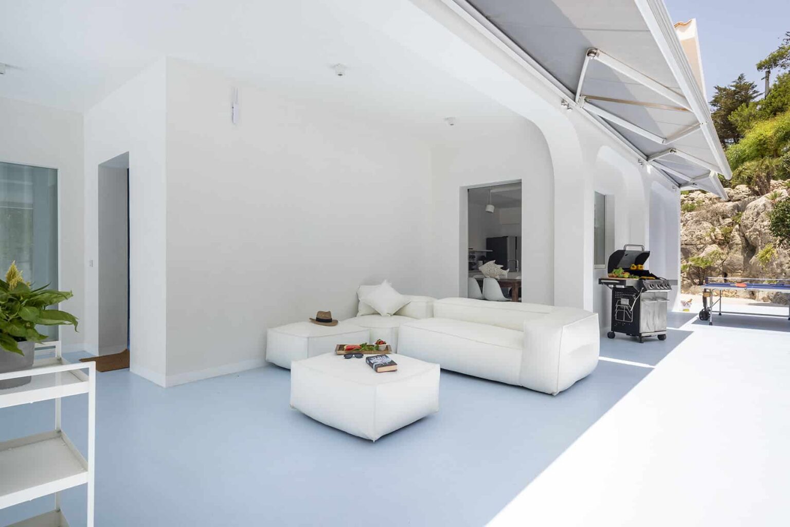 Modern white living room with minimalist furniture, featuring a spacious layout and large windows that open to an outdoor area, ideal for relaxation and entertaining. | Only on SopranoVillas