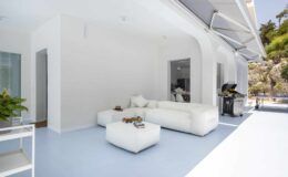 Modern white living room with minimalist furniture, featuring a spacious layout and large windows that open to an outdoor area, ideal for relaxation and entertaining.