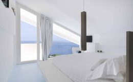 Modern bedroom with panoramic ocean view, featuring minimalist design, large windows, and soft white bedding.