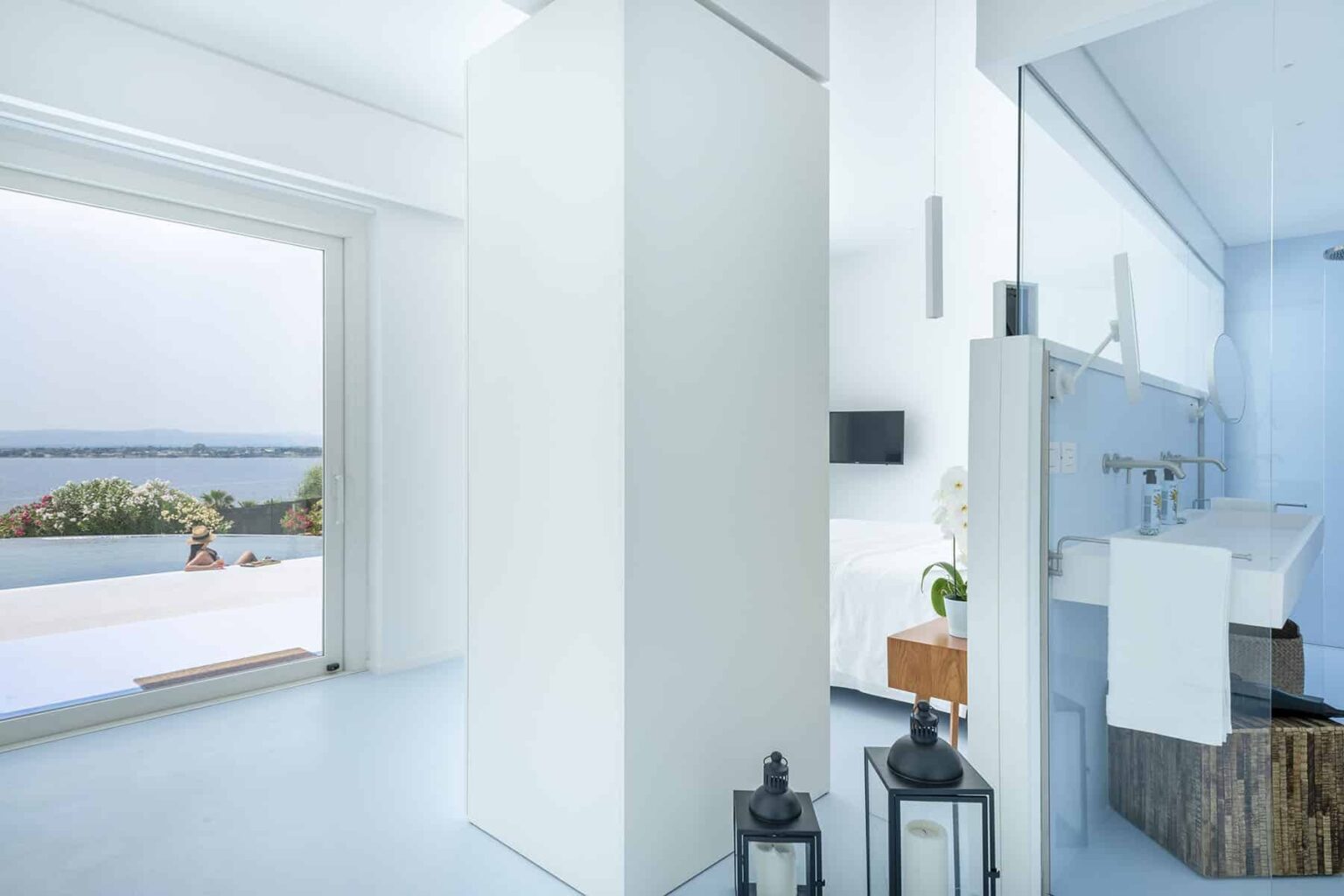 Modern interior of a bright, airy bathroom featuring white walls, a sleek design, and a view of the ocean through large windows, complemented by stylish decor elements. | Only on SopranoVillas