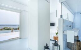 Modern interior of a bright, airy bathroom featuring white walls, a sleek design, and a view of the ocean through large windows, complemented by stylish decor elements.
