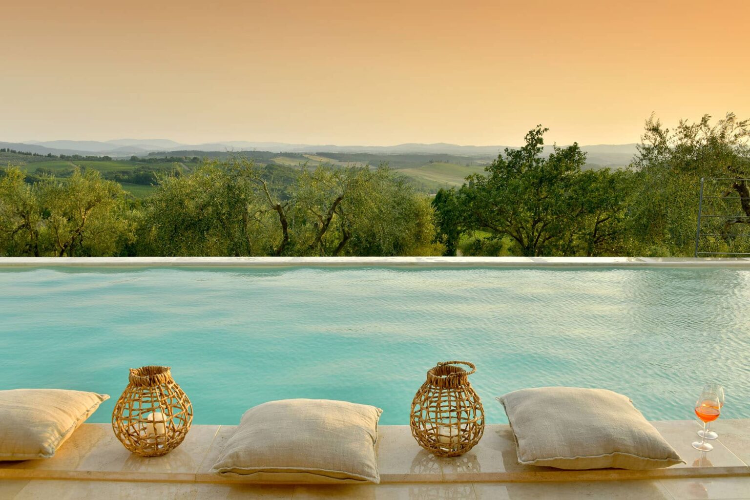 Serene infinity pool overlooking rolling hills at sunset, featuring decorative lanterns and plush cushions for relaxation. Ideal for luxury travel and wellness retreats. | Only on SopranoVillas