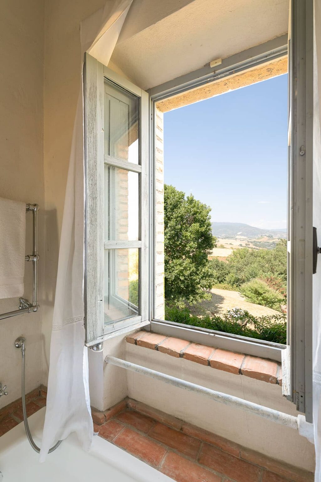 Bathroom window with a scenic view of lush greenery and distant hills, showcasing a serene countryside landscape. | Only on SopranoVillas