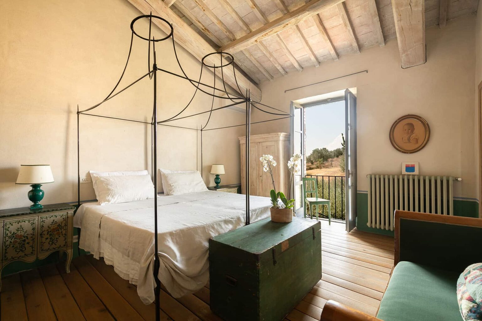 Cozy bedroom featuring a four-poster bed, natural light streaming through open French doors, and a rustic decor with wooden floors and vintage furnishings. Ideal for a relaxing getaway. | Only on SopranoVillas