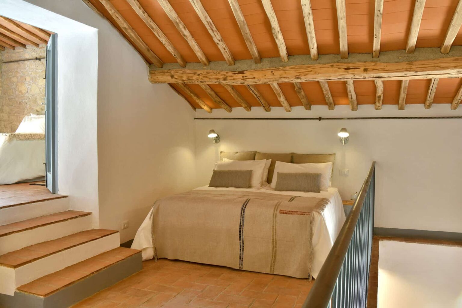 Cozy loft bedroom with wooden beams, featuring a queen-sized bed dressed in neutral-toned linens, accented by modern bedside lamps and a warm, inviting atmosphere. | Only on SopranoVillas