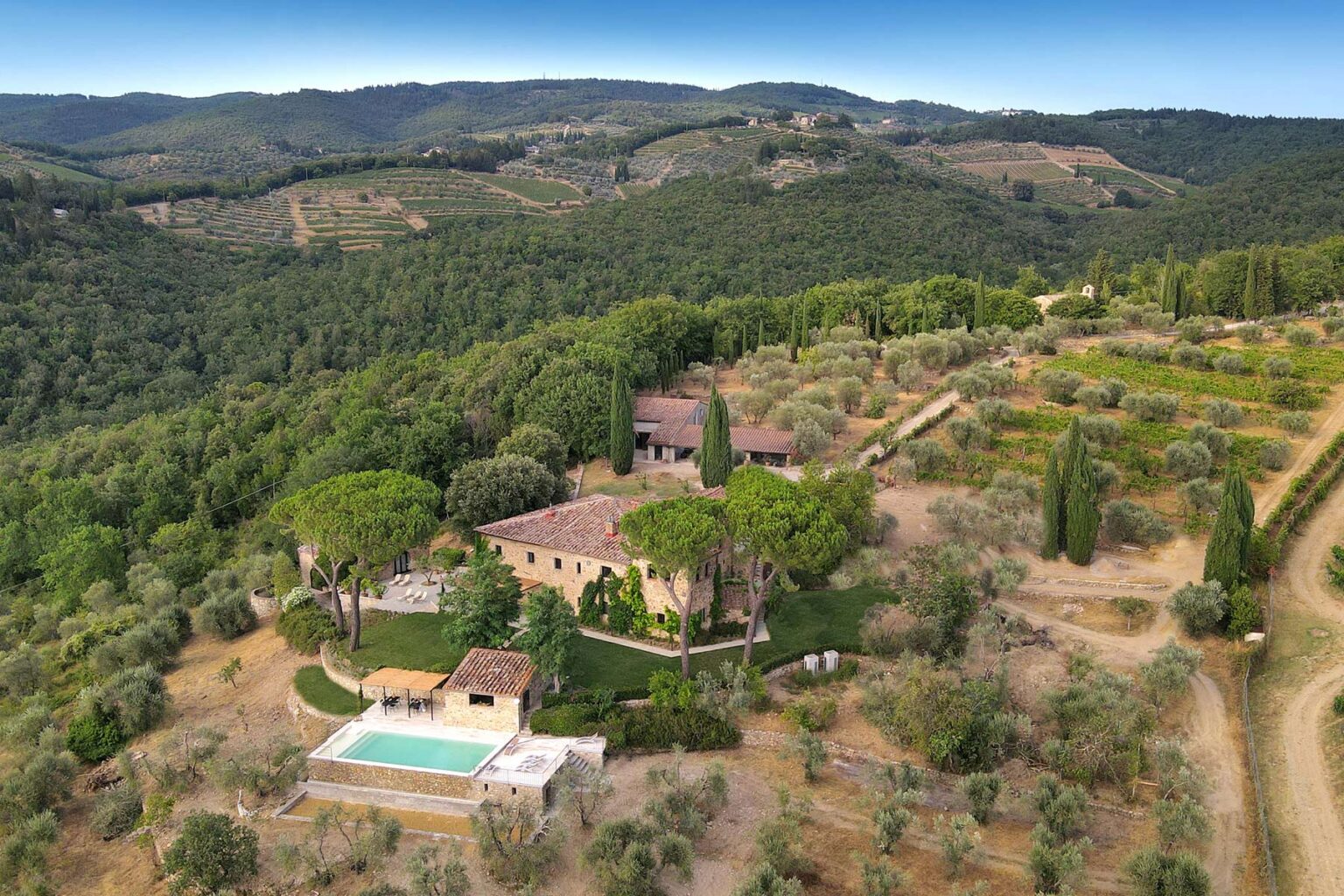 Aerial view of a picturesque villa surrounded by lush greenery and rolling hills, featuring a swimming pool and landscaped gardens, ideal for a tranquil getaway or vacation rental in a rural setting. | Only on SopranoVillas