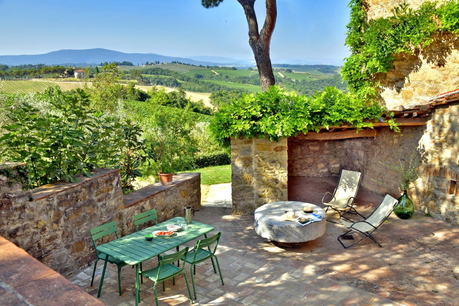 Charming outdoor patio with green table and chairs, surrounded by lush greenery and scenic hills in the background, perfect for relaxing in a tranquil countryside setting. | Only on SopranoVillas