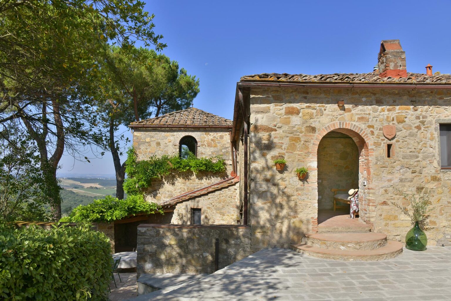 Rustic stone villa in Tuscany with terracotta roof, surrounded by lush greenery and trees, showcasing a charming entrance and scenic views. Ideal for travelers seeking a tranquil getaway in the Italian countryside. | Only on SopranoVillas