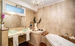 Elegant modern bathroom featuring a luxurious bathtub, dual glass sinks, and stylish decor with a chandelier and potted plants.