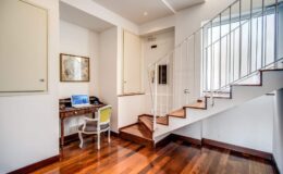 Modern home interior featuring a staircase, a small workspace with a desk and chair, and wooden flooring, creating a bright and inviting atmosphere.