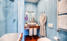 Modern bathroom featuring light blue striped walls, a bathtub, a stylish sink with a mirror, and elegant decor, including a robe and towels.