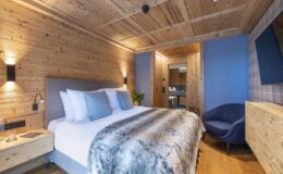 Cozy hotel room featuring a wooden interior, a plush king-sized bed with decorative pillows, a stylish chair, and modern amenities, perfect for a relaxing stay.