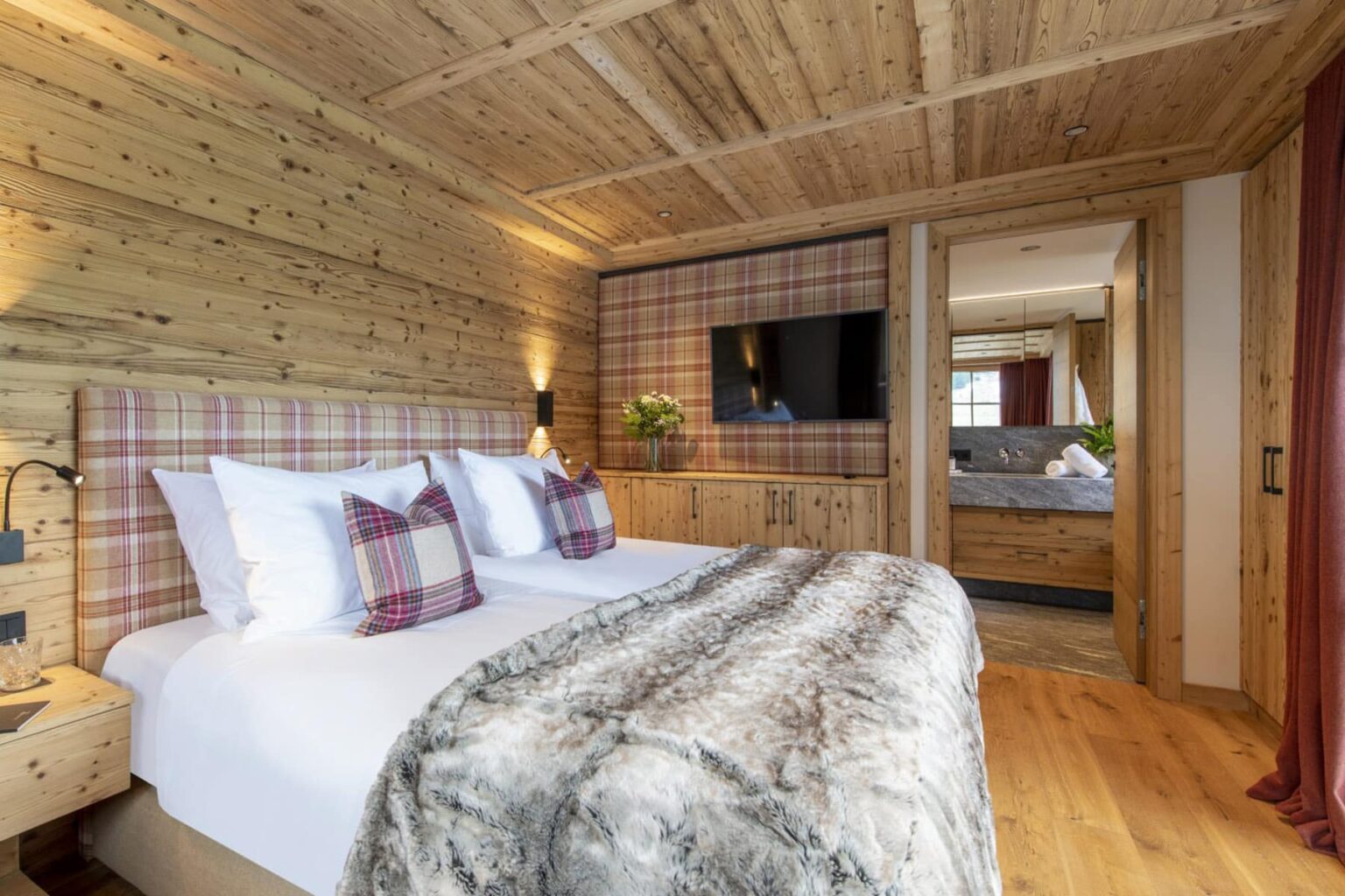 Cozy wooden bedroom featuring a double bed with plaid accents, a plush fur throw, and modern amenities, designed for comfort and relaxation in a rustic style. | Only on SopranoVillas