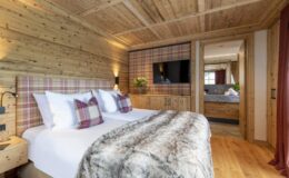 Cozy wooden bedroom featuring a double bed with plaid accents, a plush fur throw, and modern amenities, designed for comfort and relaxation in a rustic style.