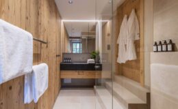 Modern bathroom design featuring wooden accents, a glass shower enclosure, plush white towels, and elegant toiletries.