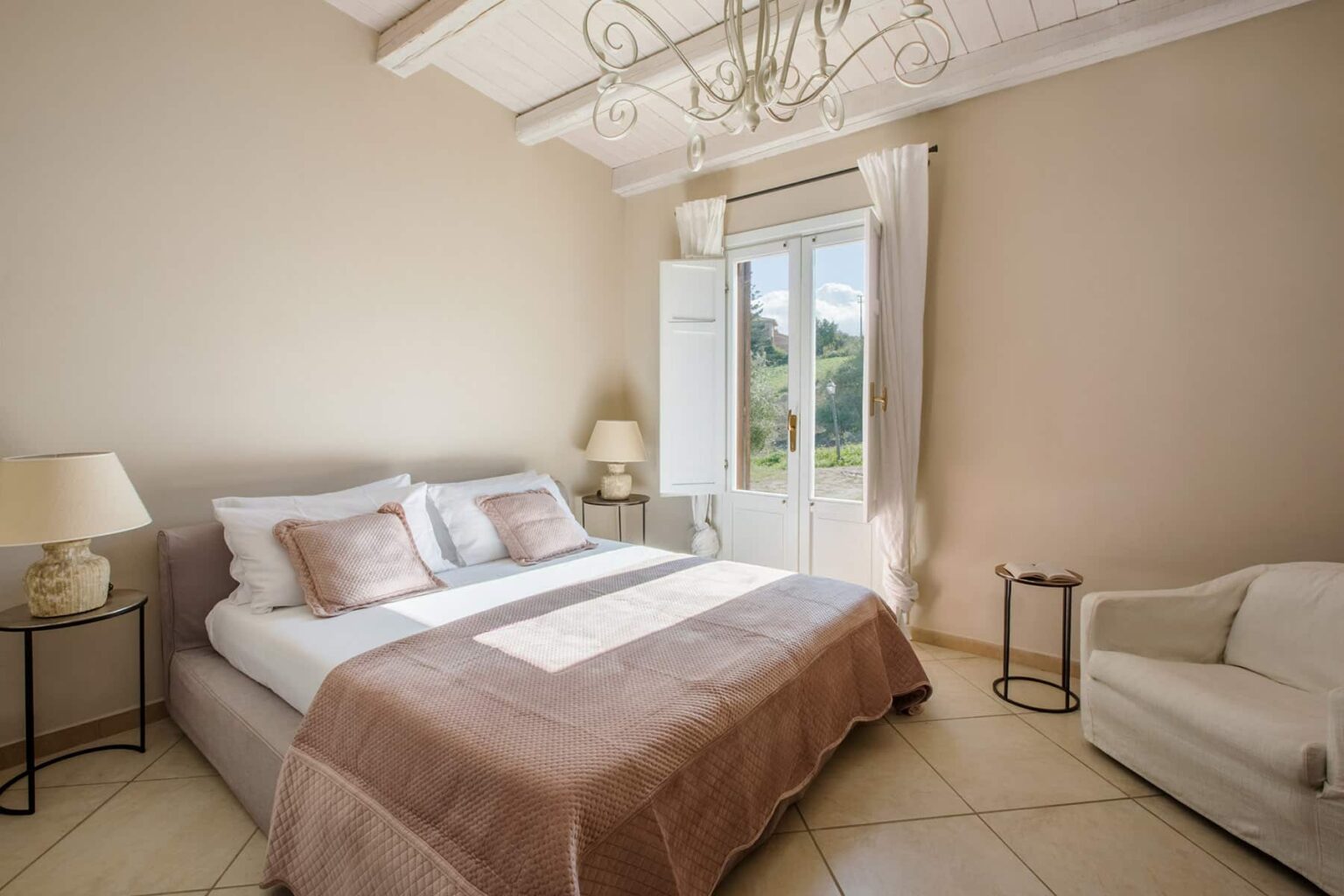 Bright and airy bedroom featuring a plush bed with neutral bedding, a cozy armchair, and large windows that let in natural light, creating a serene atmosphere. | Only on SopranoVillas