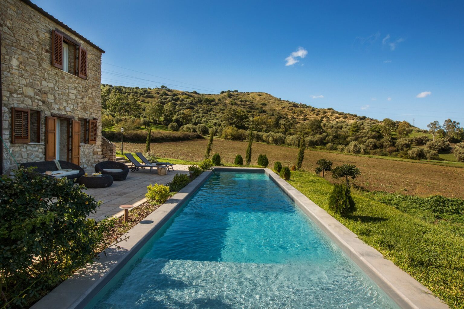Stone villa with a swimming pool surrounded by lush greenery and rolling hills under a clear blue sky. Ideal for luxury retreats and outdoor relaxation. | Only on SopranoVillas