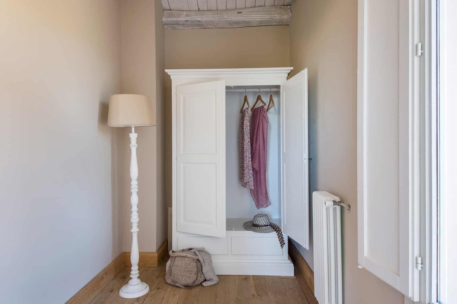 Interior view of a stylish white wardrobe with open doors, featuring hanging clothes, a floor lamp, and a cozy atmosphere in a modern hallway. | Only on SopranoVillas