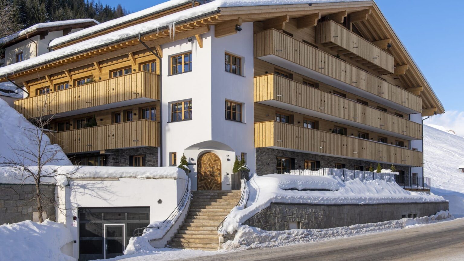 Modern alpine hotel exterior featuring wooden balconies and snow-covered surroundings, ideal for winter getaways. | Only on SopranoVillas