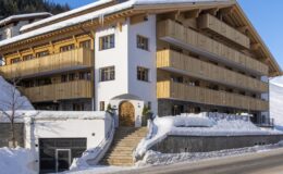 Modern alpine hotel exterior featuring wooden balconies and snow-covered surroundings, ideal for winter getaways.