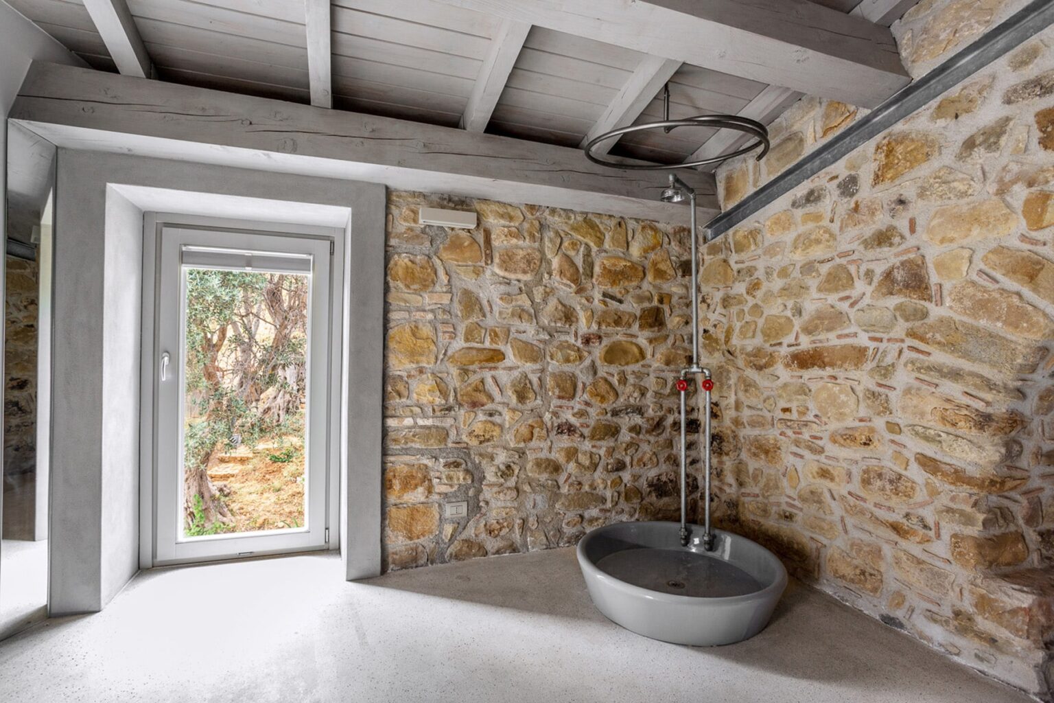 Modern bathroom featuring natural stone walls, minimalist design, and a round shower basin. Large window provides natural light and views of the outdoors. | Only on SopranoVillas
