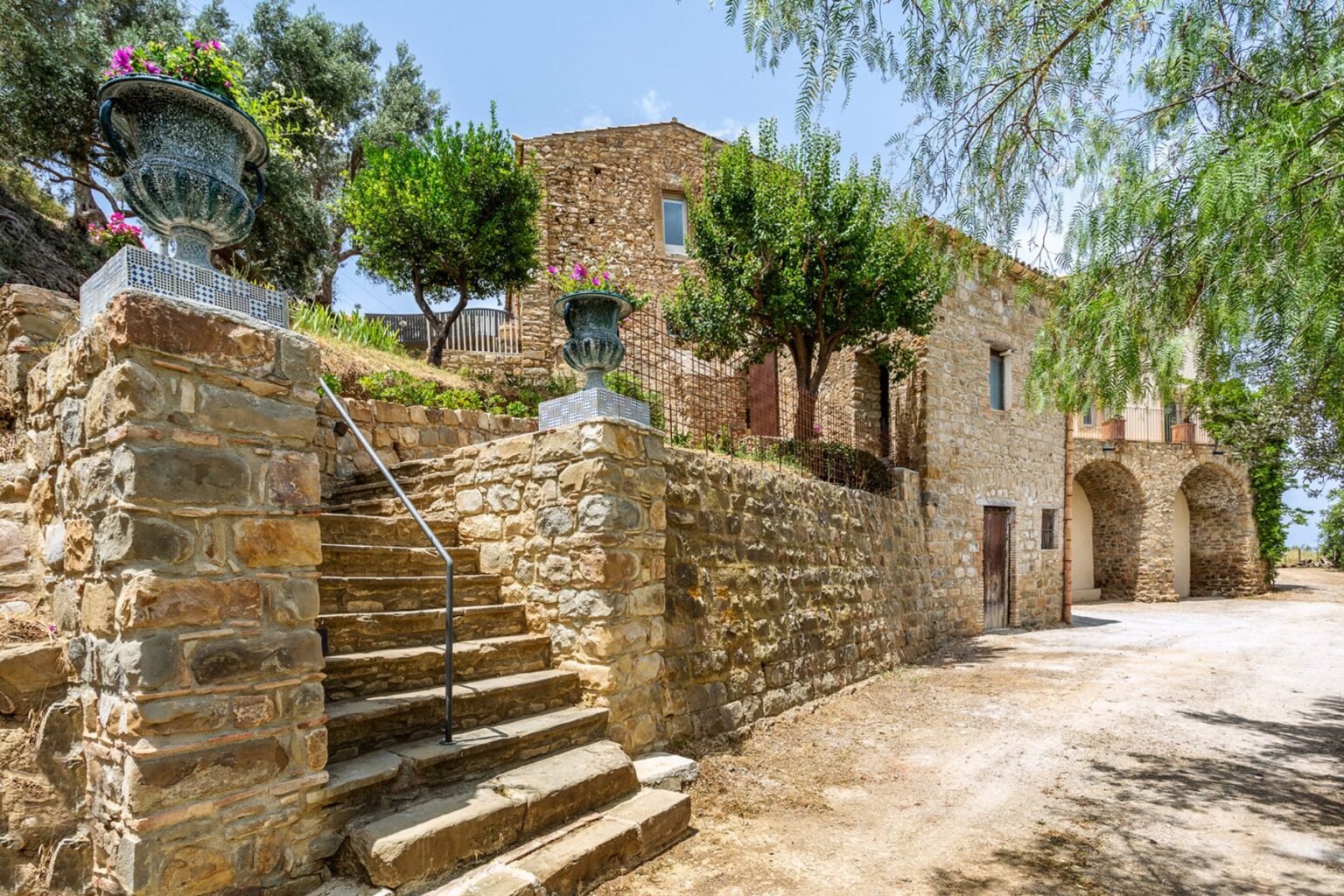 Stone villa with lush greenery and steps leading to the entrance, set in a serene landscape. Ideal for vacation rentals or countryside retreats. | Only on SopranoVillas