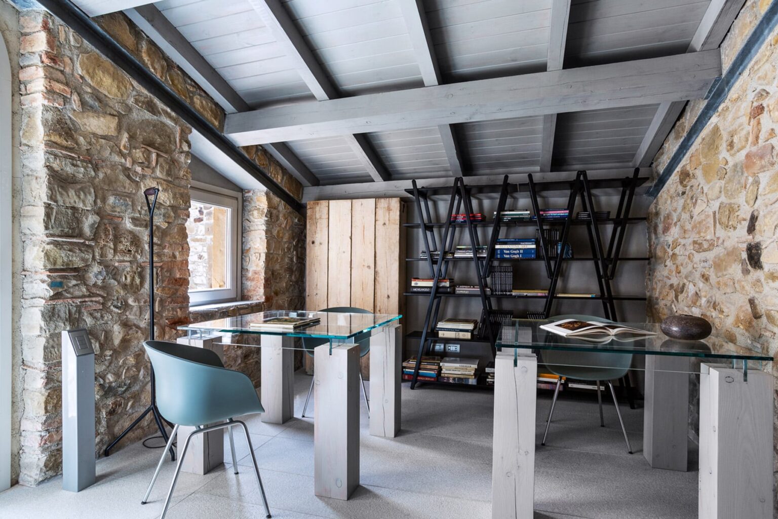Modern office interior featuring glass desks, a minimalist chair, and a stylish bookshelf against stone walls and wooden beams. Ideal for contemporary workspace design inspiration. | Only on SopranoVillas