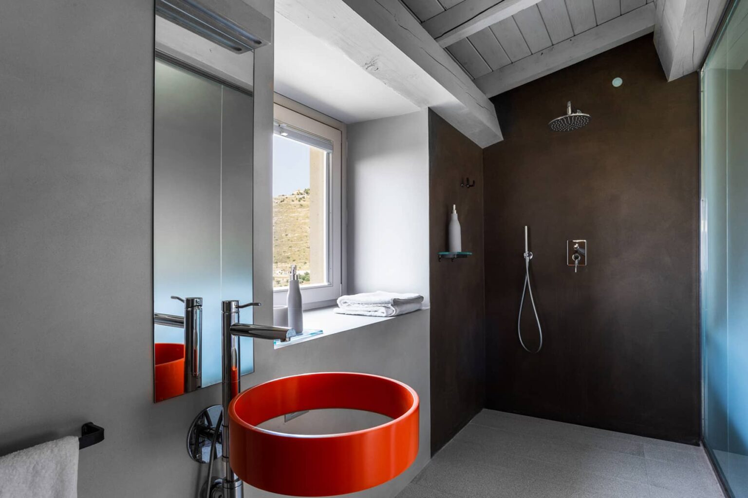 Modern bathroom featuring a sleek design with a shower area, large window for natural light, and a striking orange circular sink. The interior combines neutral tones with contemporary fixtures for a stylish look. | Only on SopranoVillas