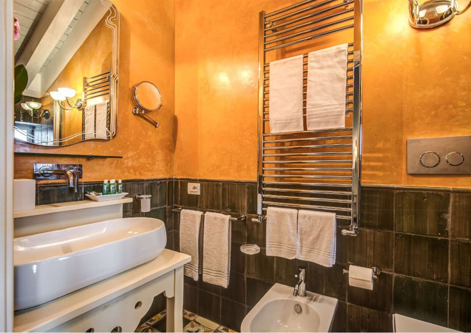 Modern bathroom interior featuring a stylish sink, heated towel rack, and decorative wall. The space is adorned with warm orange tones and elegant fixtures, creating a cozy atmosphere. | Only on SopranoVillas
