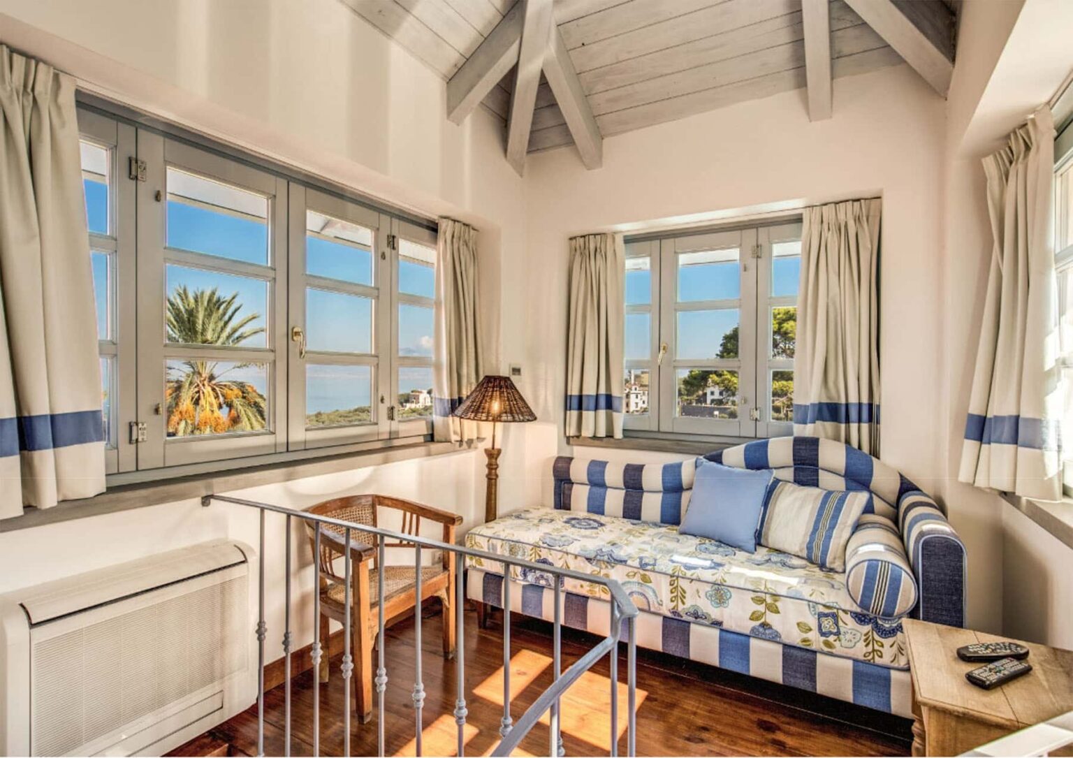 Cozy living space featuring a striped daybed, large windows with scenic views, and light-colored walls, perfect for relaxation and natural light. | Only on SopranoVillas