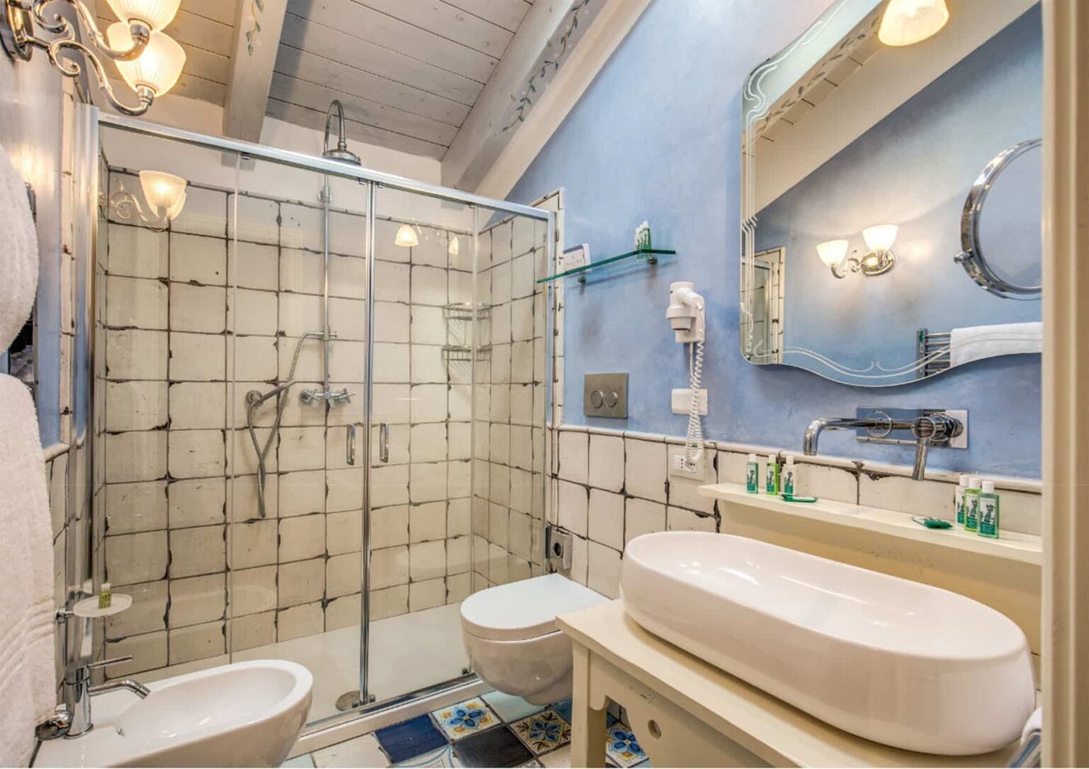 Modern bathroom featuring a glass shower enclosure, stylish sink, and elegant lighting against a blue wall with tiled accents, designed for functionality and aesthetics. | Only on SopranoVillas