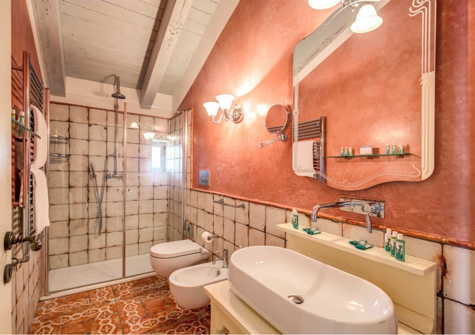 Modern bathroom featuring a walk-in shower with glass enclosure, dual sinks, stylish fixtures, and warm-toned walls. The space includes a bidet and decorative mirror, creating an inviting atmosphere. | Only on SopranoVillas