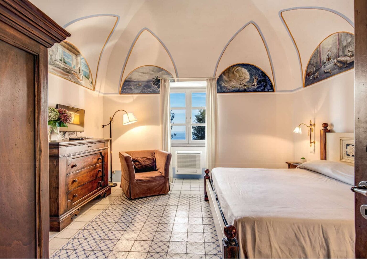 Cozy bedroom with arched ceilings and elegant decor, featuring a comfortable bed, wooden furniture, and a large window offering scenic views. Perfect for a relaxing getaway. | Only on SopranoVillas