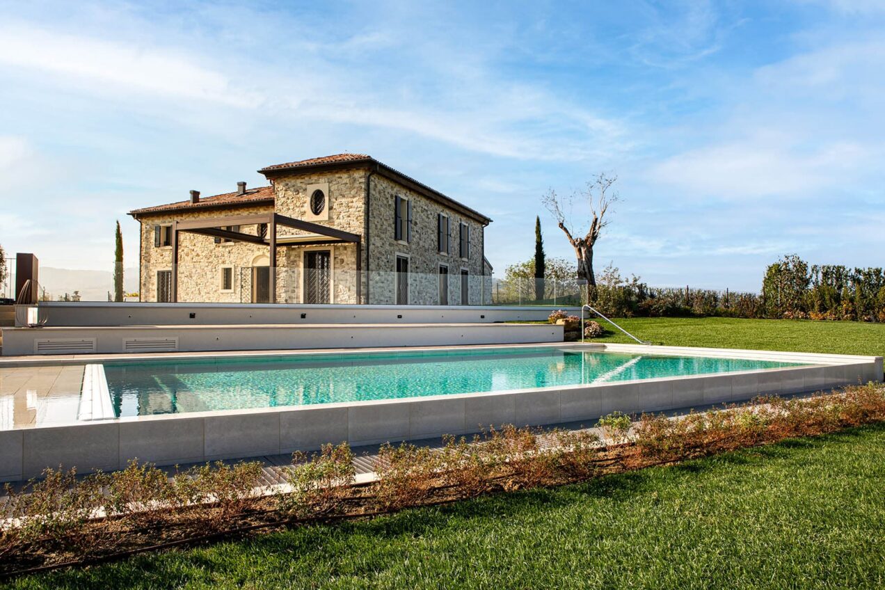 Luxury stone villa with a modern pool, surrounded by lush greenery and scenic views under a clear blue sky. Ideal for relaxation and vacation getaways.