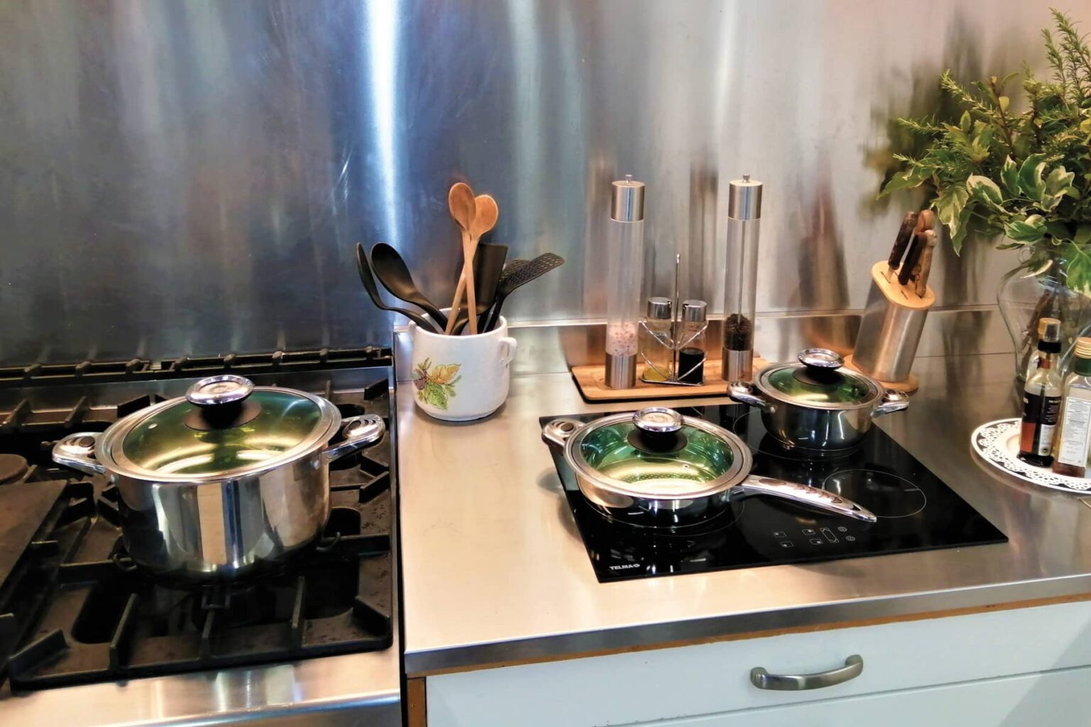 Modern kitchen with stainless steel appliances, featuring two pots simmering on a gas stove. Wooden cooking utensils and spice containers are neatly arranged on the countertop, showcasing a clean and organized cooking space. | Only on SopranoVillas