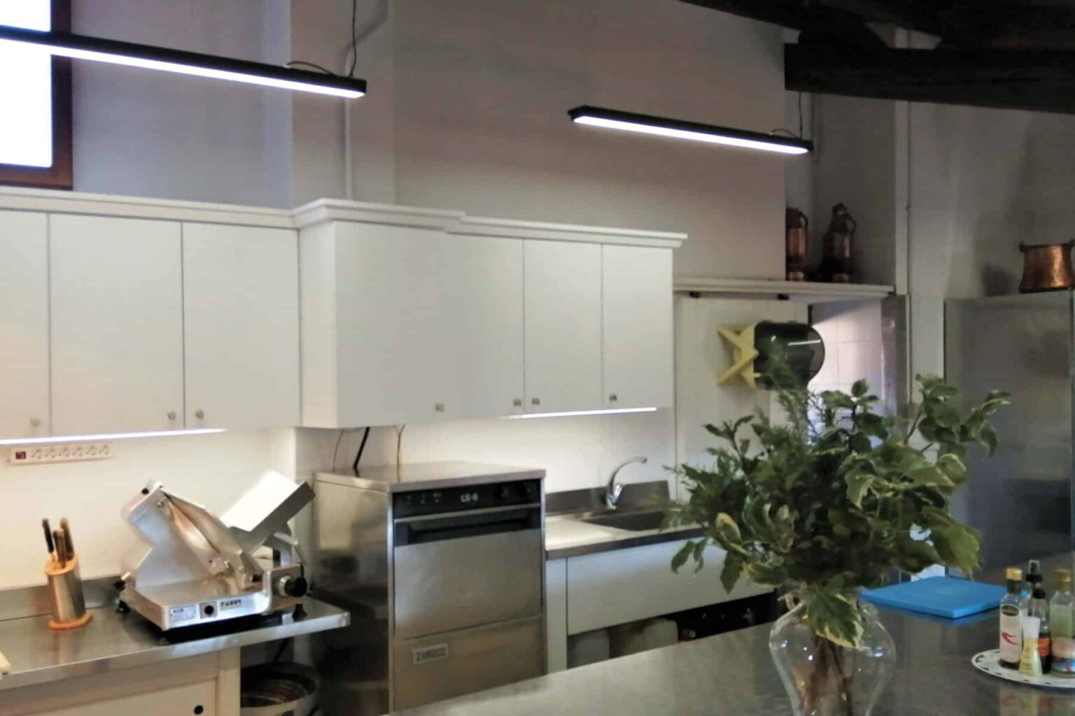 Modern kitchen with white cabinetry, stainless steel appliances, and a vase of greenery on the countertop, featuring under-cabinet lighting for enhanced visibility. | Only on SopranoVillas