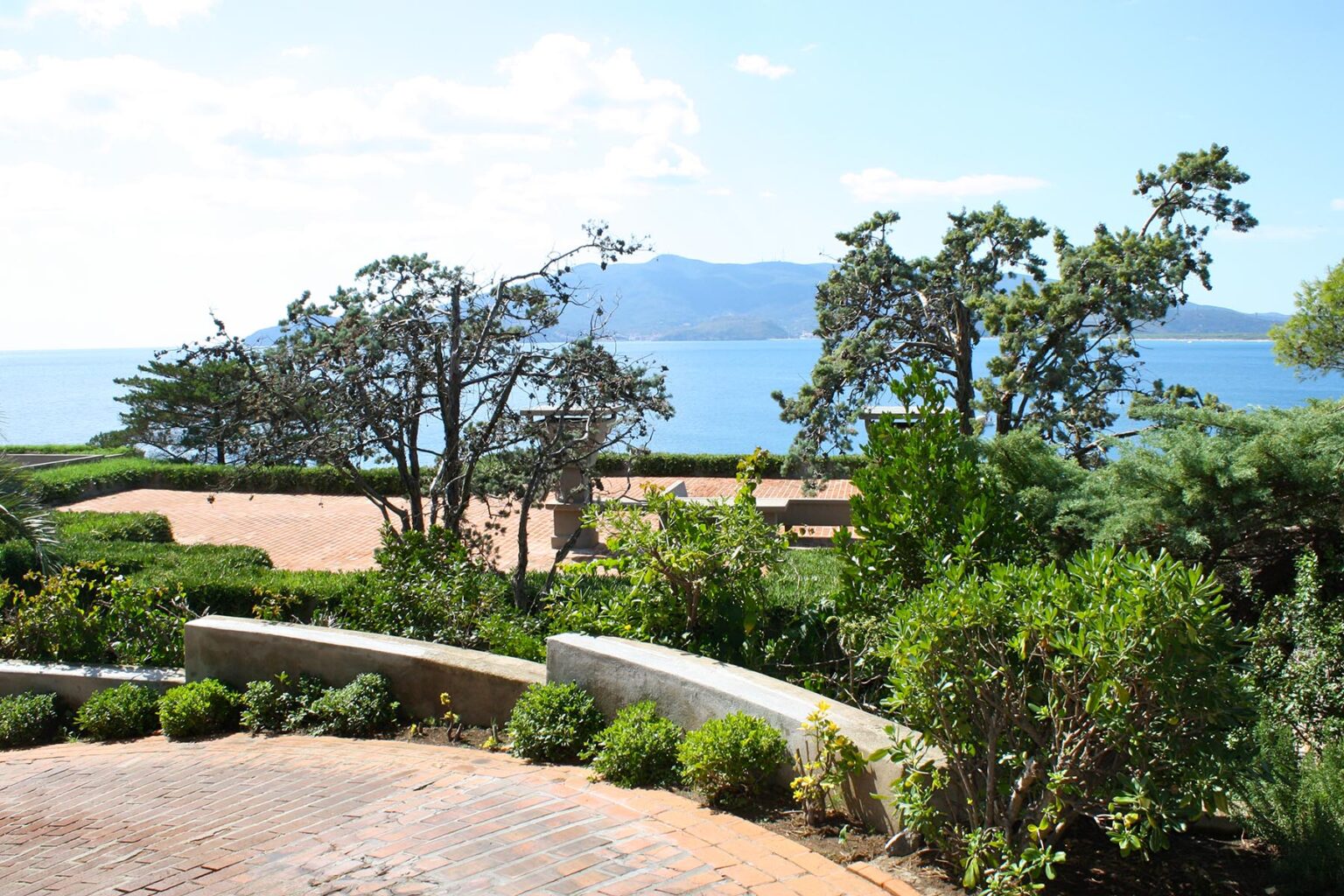 Scenic view of a landscaped garden overlooking a tranquil lake with mountains in the background under a clear blue sky. | Only on SopranoVillas