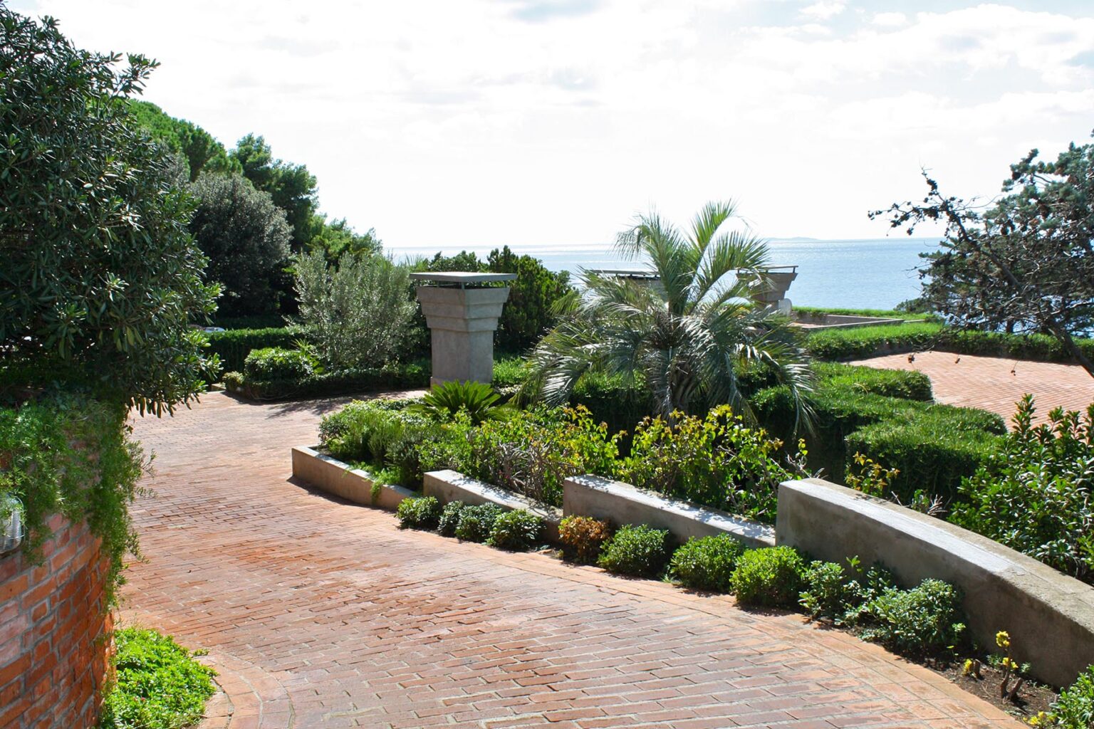 Scenic pathway leading through lush greenery and vibrant flowers, with a view of the ocean in the background, showcasing a tranquil outdoor setting. | Only on SopranoVillas