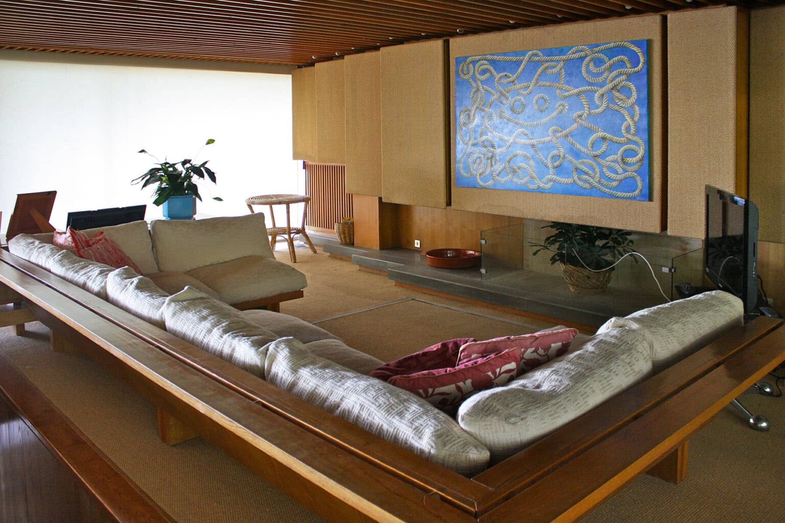 Modern living room interior featuring a low wooden table with cushions, minimalist decor, a large blue artwork on the wall, and a potted plant, creating a serene and stylish atmosphere. | Only on SopranoVillas