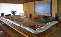 Modern living room interior featuring a low wooden table with cushions, minimalist decor, a large blue artwork on the wall, and a potted plant, creating a serene and stylish atmosphere.