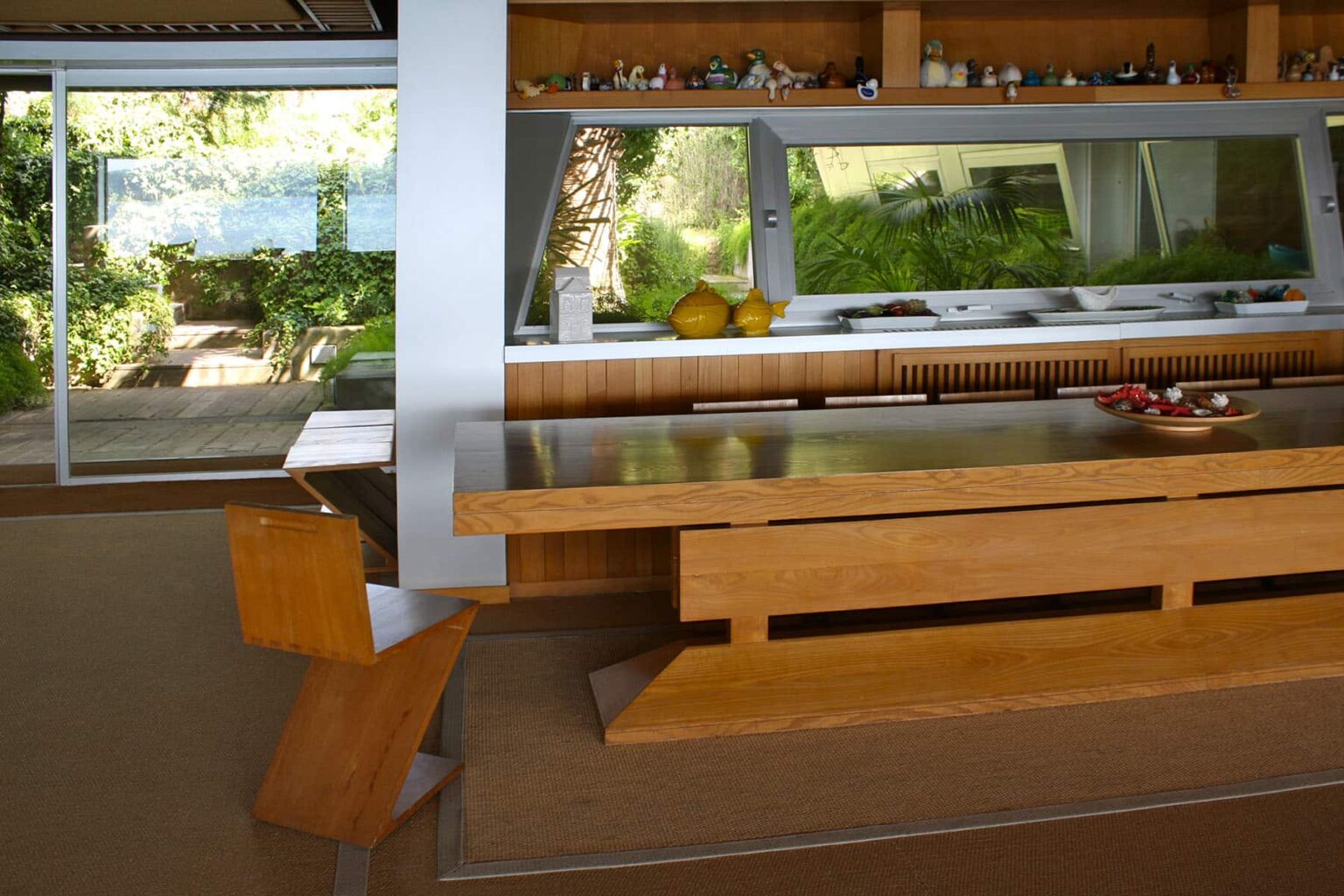 Modern kitchen interior featuring a sleek wooden dining table, minimalist design, and large windows that provide natural light and views of greenery outside. | Only on SopranoVillas