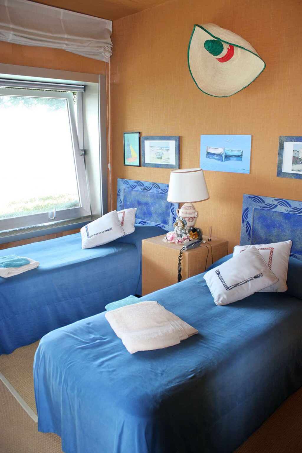 Cozy bedroom featuring two twin beds with blue bedding, a bedside table with a decorative lamp, and framed artwork on the walls, creating a serene and inviting atmosphere. | Only on SopranoVillas