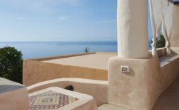 Cozy outdoor terrace with stunning ocean view, featuring a tiled table and natural stone architecture, perfect for relaxation and enjoying coastal scenery.
