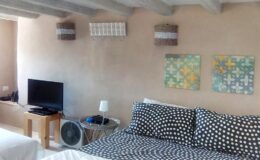Cozy bedroom interior featuring a polka dot bedspread, wall-mounted art, a television, and decorative wall sconces, with a rustic charm enhanced by exposed wooden beams.