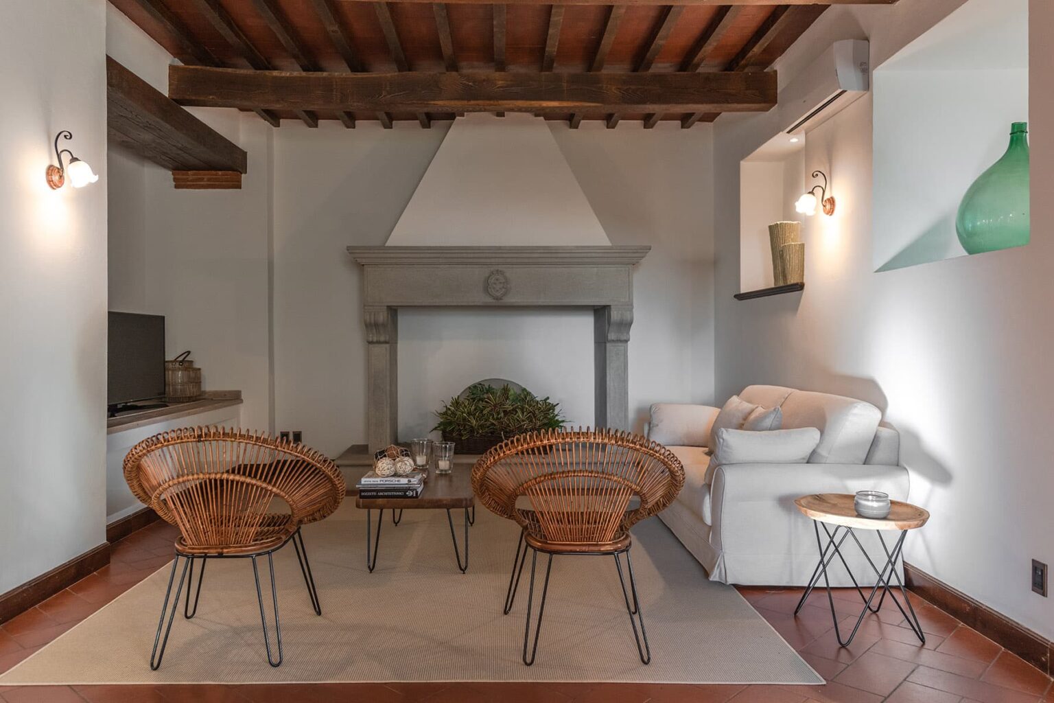 Cozy living room featuring a white sofa, wicker chairs, and a stone fireplace, complemented by wooden beams and soft lighting for a warm atmosphere. | Only on SopranoVillas