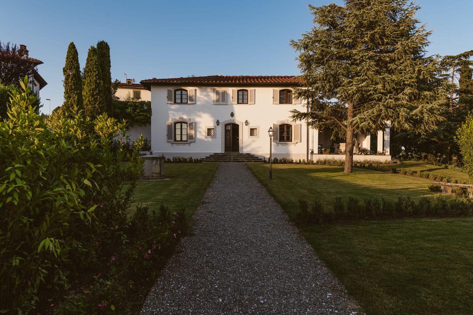 Charming white villa with a gravel pathway surrounded by lush greenery and trees, ideal for a serene getaway or vacation rental. | Only on SopranoVillas